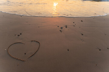 Hearth symbol on sand against a background of sunset over the sea