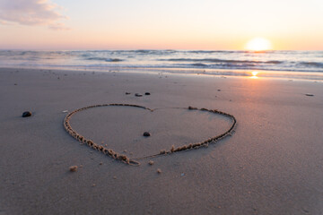 Hearth symbol on sand against a background of sunset over the sea