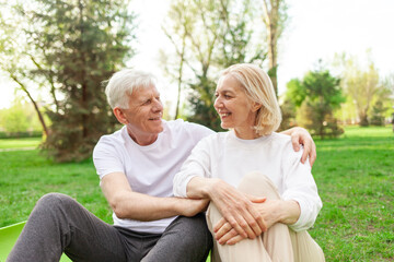 elderly couple of seniors man and woman hugging and smiling in the park outdoors, gray-haired grandparents in white T-shirts in nature