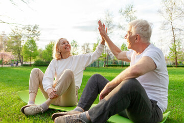elderly couple of seniors man and woman high-five and rejoice at success in the park outdoors, gray-haired grandparents celebrate victory and play sports in nature
