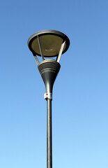 Street lamp light mounted on a slender pole against a clear blue sky