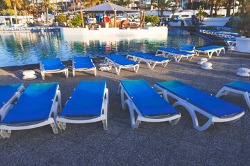 Fototapeta na wymiar Lounge chairs by a pool, perfect for relaxing under the sun on vacation. Poolside lounge chairs