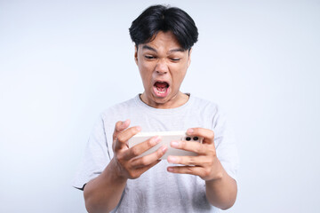 Potrait Of Annoyed Young Asian Guy Playing Game On Smartphone And Screaming Isolated On White...