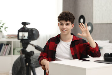 Smiling teenage blogger waving hello to his subscribers while streaming at home
