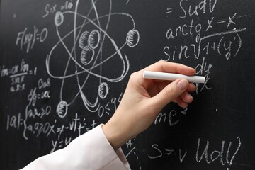 Teacher writing math formulas with chalk on blackboard, closeup