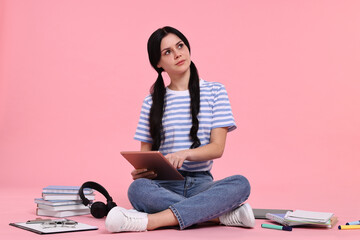Student with tablet sitting among books and stationery on pink background