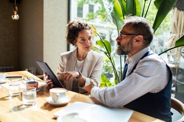 Two colleagues discussing work with tablet over coffee in a cafe