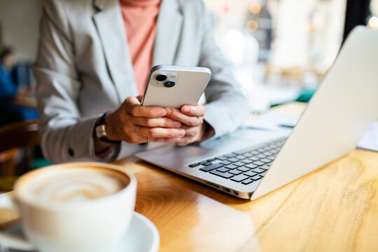Close up of a businesswoman using smartphone and laptop in a cafe