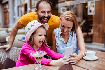 Happy family enjoying time together with smartphone at outdoor cafe