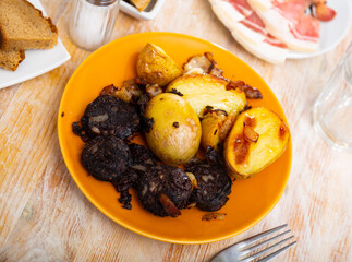Delicious fried blood sausage served with potato slices and onions on plate