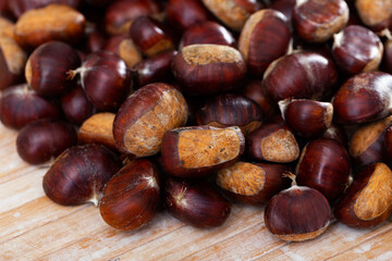 Closeup of heap of dark brown edible chestnuts on wooden background..
