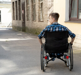 Obraz premium A young disabled man sits in a wheelchair and listens to music on headphones. Walk on a summer day.