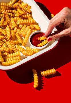 Hand dipping crinkle cut chips into tomato sauce