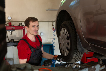 a mechanic stands by a car in a car service center. master removes a wheel from a car, repair,...