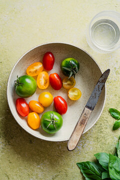 Bowl of small, coloured charry and plum tomatoes  with a small knife on green background
