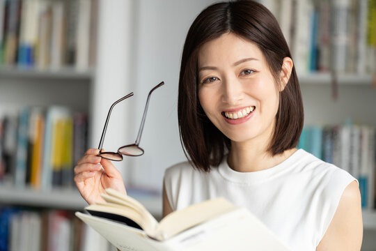本棚の前でメガネを持って本を持っている女性