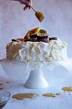 Traditional Australian Pavlova Dessert with Fresh Figs and Served with Honey. Female hand with honey drizzler.