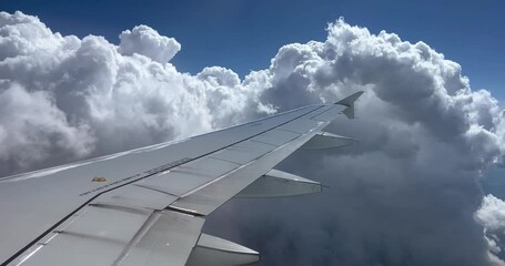 Passenger Point of view of airplane wing flying through white fluffy clouds on a bright sunny day. Airplane window view with wing and clouds.