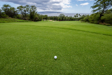 Golf ball on tee, hole in the distance backed by the pacific ocean, tropical golf vacation, Maui,...