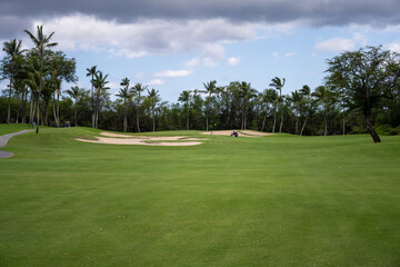 Fairway leading to hole protected by sand traps, golfer and cart close to the green, tropical golf...