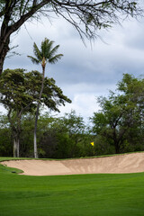Yellow flag on green protected by sand traps, storm clouds in the background, tropical golf vacation, Maui, Hawaii
