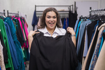 A fat woman in a plus size store tries on a black evening dress. Vertical photo. 