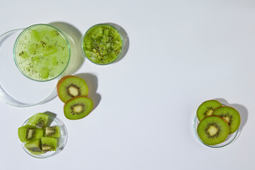 Glassware displaying fresh kiwi in form of chopped or sliced above, against white background. Vacant space in center for displaying beauty care product has natural ingredient like kiwi, top view