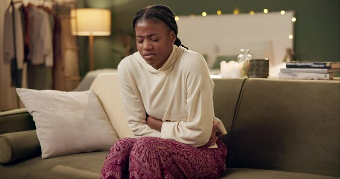 African woman, menstruation and stomach ache on sofa for pain, stress and cramps at night in living room. Girl, person and sore abdomen with virus, constipation or ibs on lounge couch in home