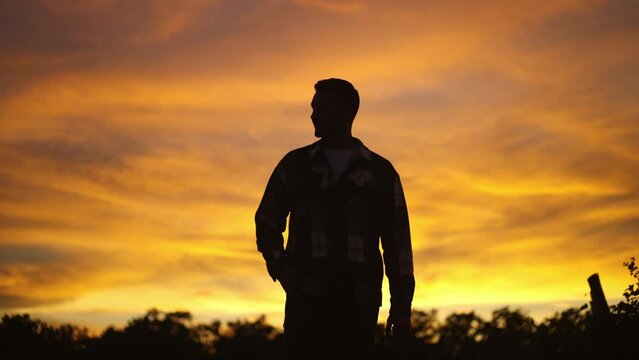 Silhouette of a young man walking through a field in slow-motion with the sunset behind him