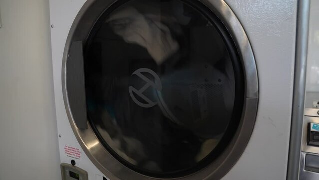 Side loader dryer machine spins with clothes dropping and tumbling in laundromat