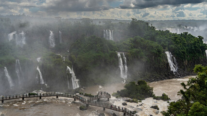 Breathtaking waterfall landscape. A tourist observation platform passes over a stormy river. People...