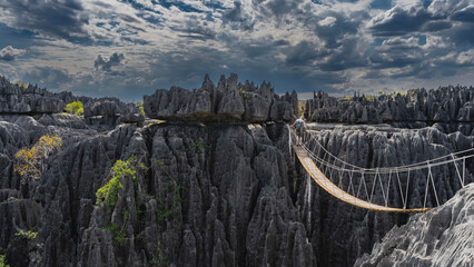A suspended wooden bridge with cable railings is spans over the abyss. Impressive sheer karst...