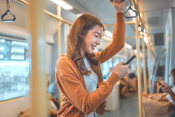 Happy young Asian woman passenger smile and using smart mobile phone in subway train station, lifestyle, transportation.