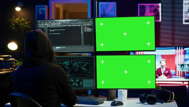Hooded man writing lines of code on green screen PC from apartment, trying to get past security systems. Evil hacker using mockup computer to make scripts that can hack devices, camera A