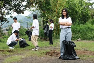 Helpful female volunteer smiling with other people picking up trash in the park. Volunteer Community Service.