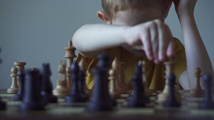 The child is a boy playing chess alone at the board. The process of thinking about a move to checkmate