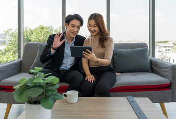 A man and woman waving hand via remote communication through tablet computer monitor  while sit on...