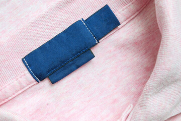 Blank blue laundry care clothes label on pink shirt fabric texture background