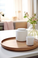 A white tea pot sits on a wooden tray next to a vase of flowers. The tray is placed on a counter in a kitchen