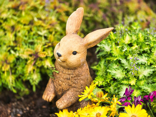 Garden ornament, garden statue, a beige bunny peeking out of the bushes.