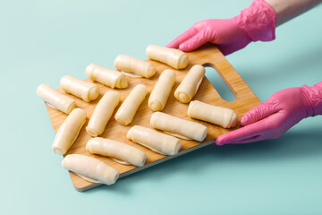 The hands of the pastry chef hold a wooden board on which raw sweet dough rolls lie neatly on a...