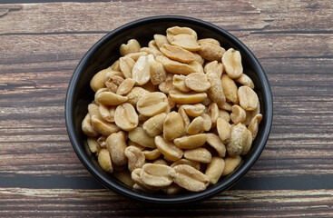 Pealed Peanuts in a black bowl isolated on wooden background