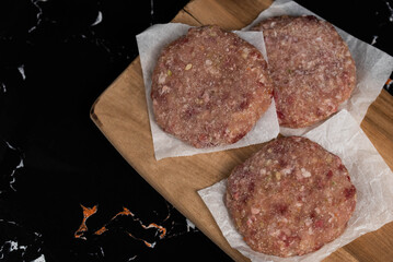 Frozen meat cutlets on dark black background, semi-finished, ready for cooking. Convenience and homemade frozen healthy meals.
