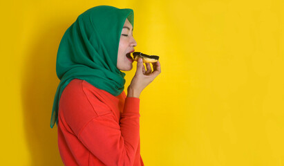 Side View Of Asian Muslim Woman Eating Donut Over Yellow Background With Copy Space