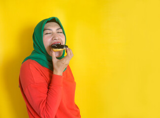Young Asian Woman Biting Eating Donuts Isolated Over Yellow Background With Copy Space