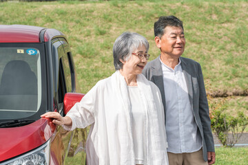 ドライブ・旅行に来た自動車の前に立つ笑顔のシニア夫婦

