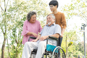 Happy asian family walking relax in the park together with smile on face during male elderly sit on wheelchair caring by his son and wife