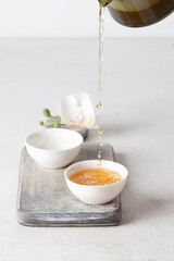 Teapot pouring green tea into the cup on wooden try. Asian tea ceremony set