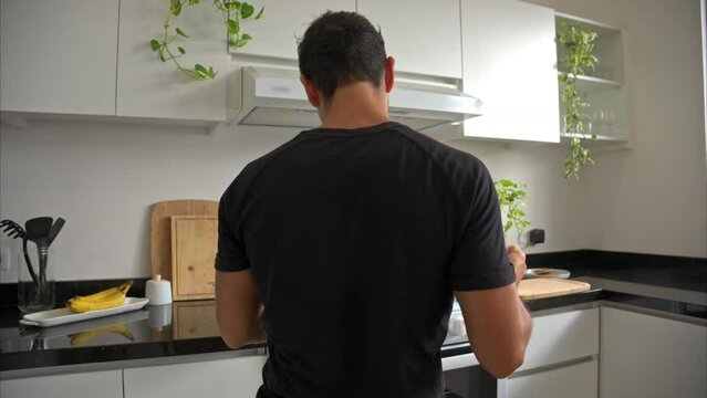Slow motion of a mexican latin fit man cooking while listening to a song dancing and singing having a great moment alone