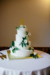 Three-tiered white wedding cake with green leaves, white flowers